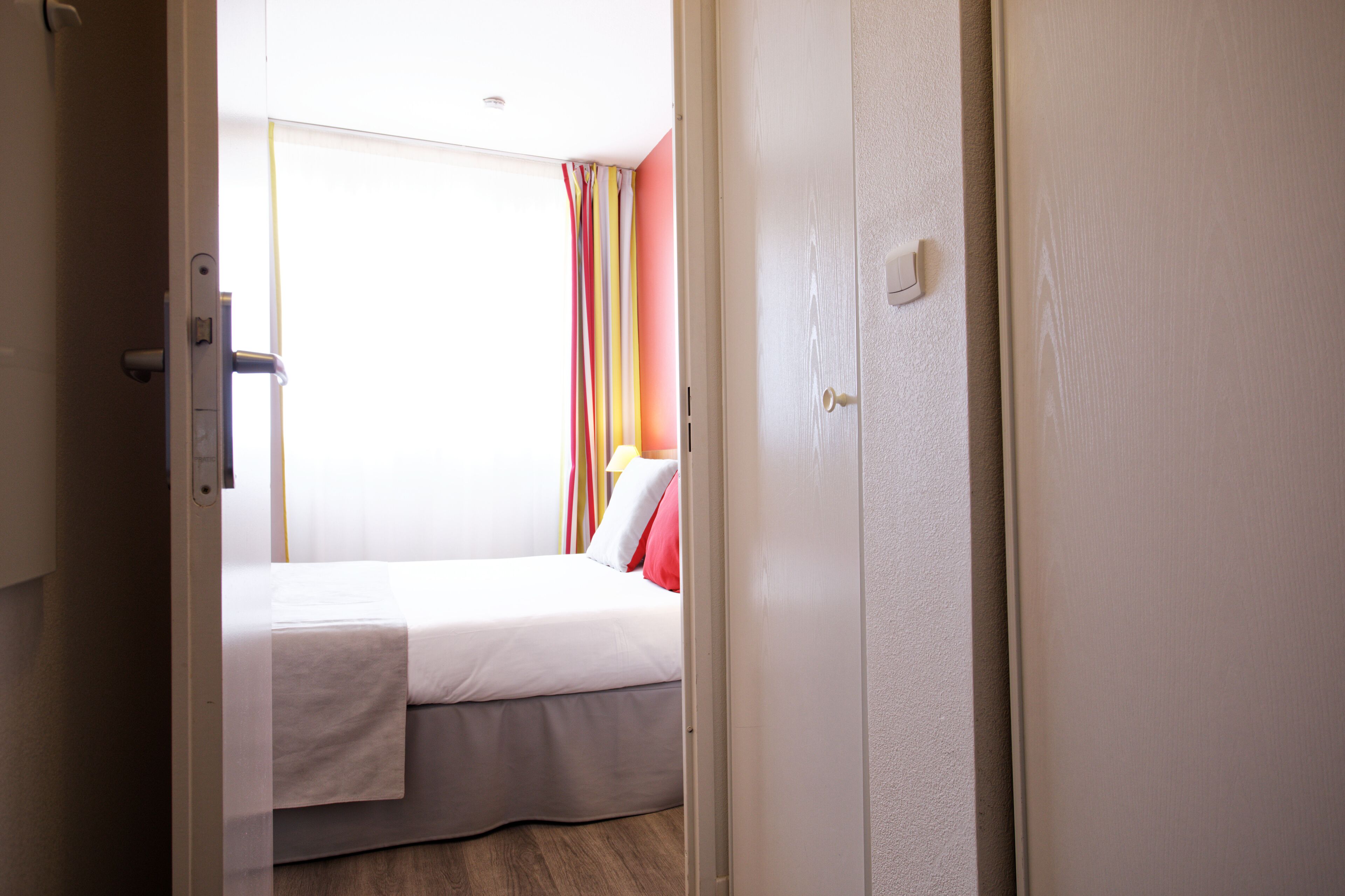 Una habitación de hotel con cama, una puerta y un ventanal con cortinas.