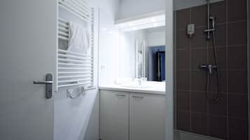 A bathroom with a white vanity, a mirror, a towel rack, and a shower area.
