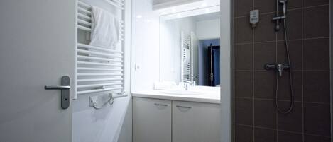 A bathroom with a white vanity, a mirror, a towel rack, and a shower area.