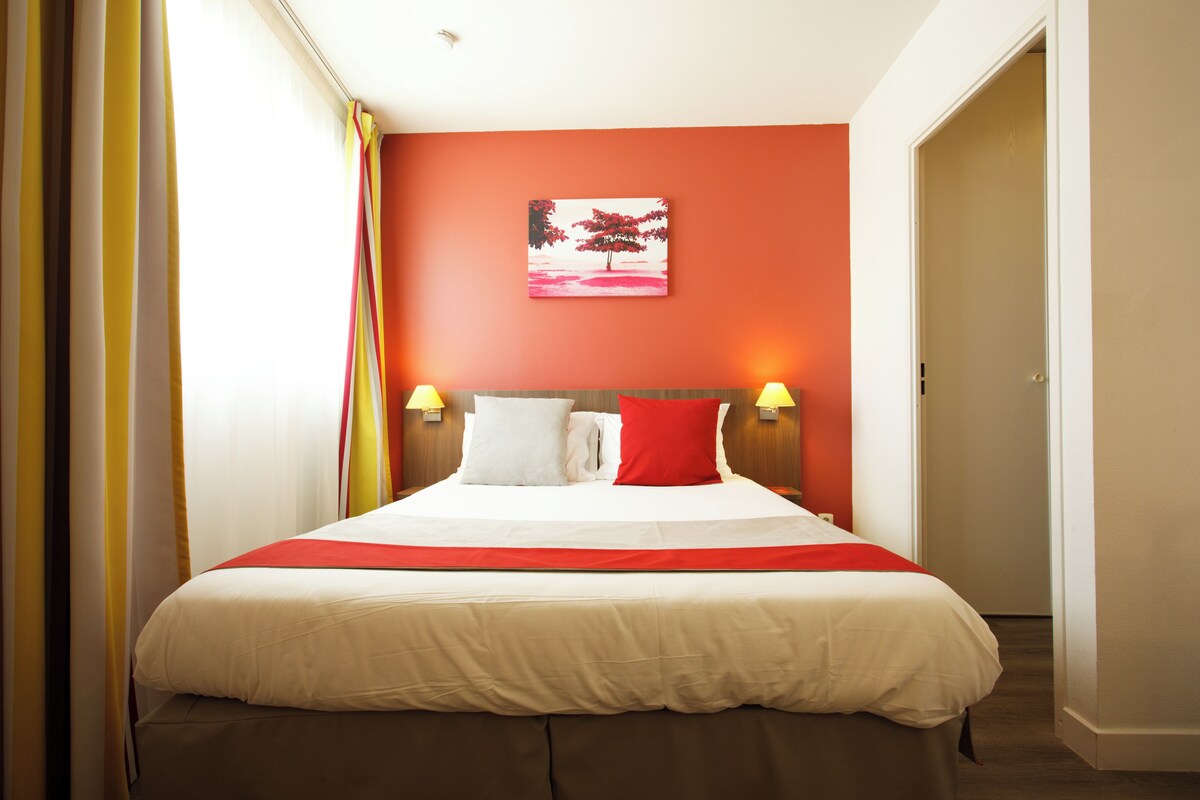 A hotel room with a large bed, red and white bedding, a red wall, and two bedside lamps.
