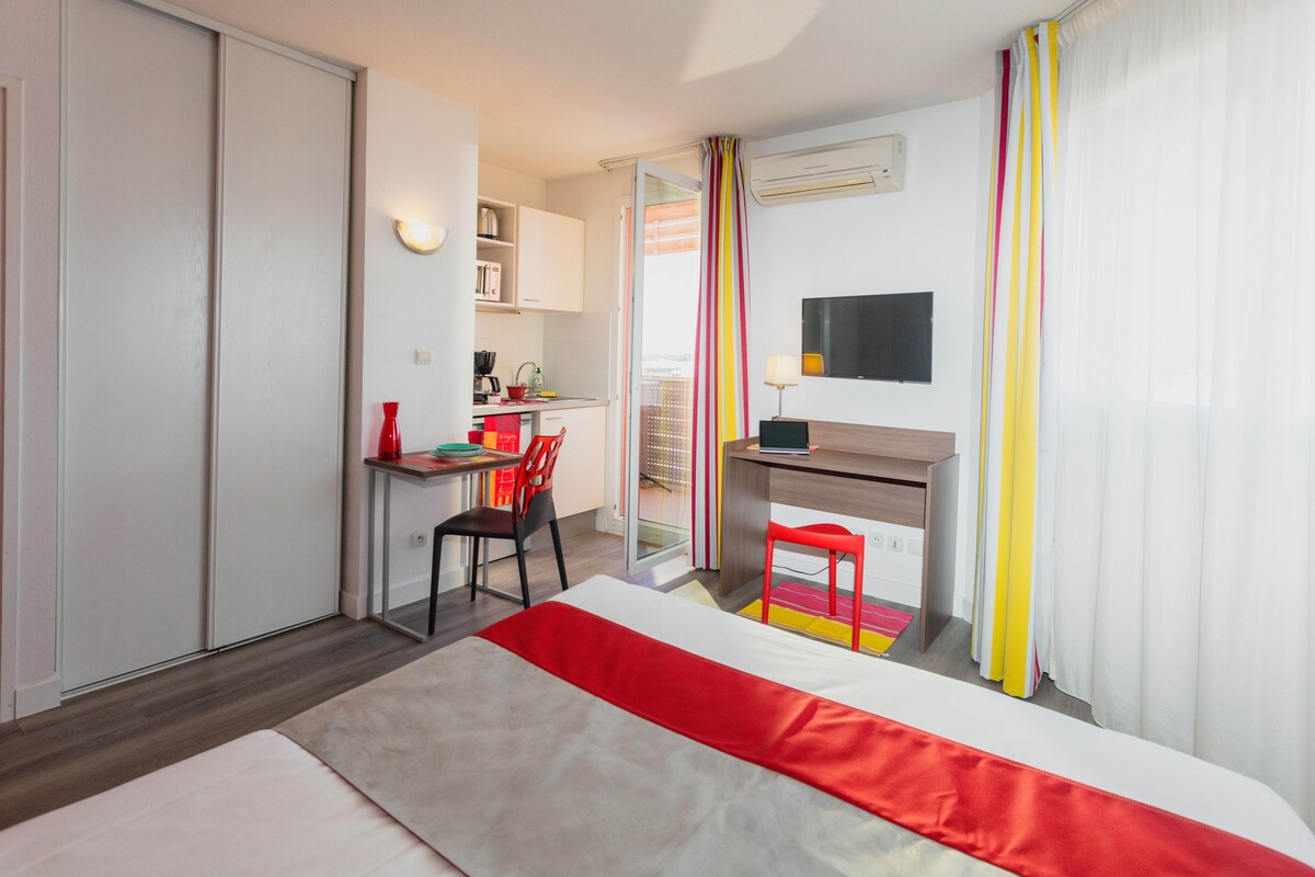 A hotel room with a bed, a desk, a chair, a TV, and a wardrobe.