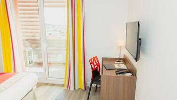 Habitación de hotel con cama, escritorio, silla, televisión y vistas a la ciudad a través del ventanal.