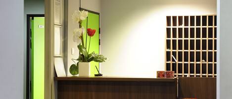 A reception area with a wooden counter, a potted plant with flowers, a green door, and a bulletin board.
