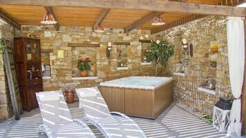 A stone-walled outdoor area with a hot tub, two lounge chairs, and a wooden cabinet.