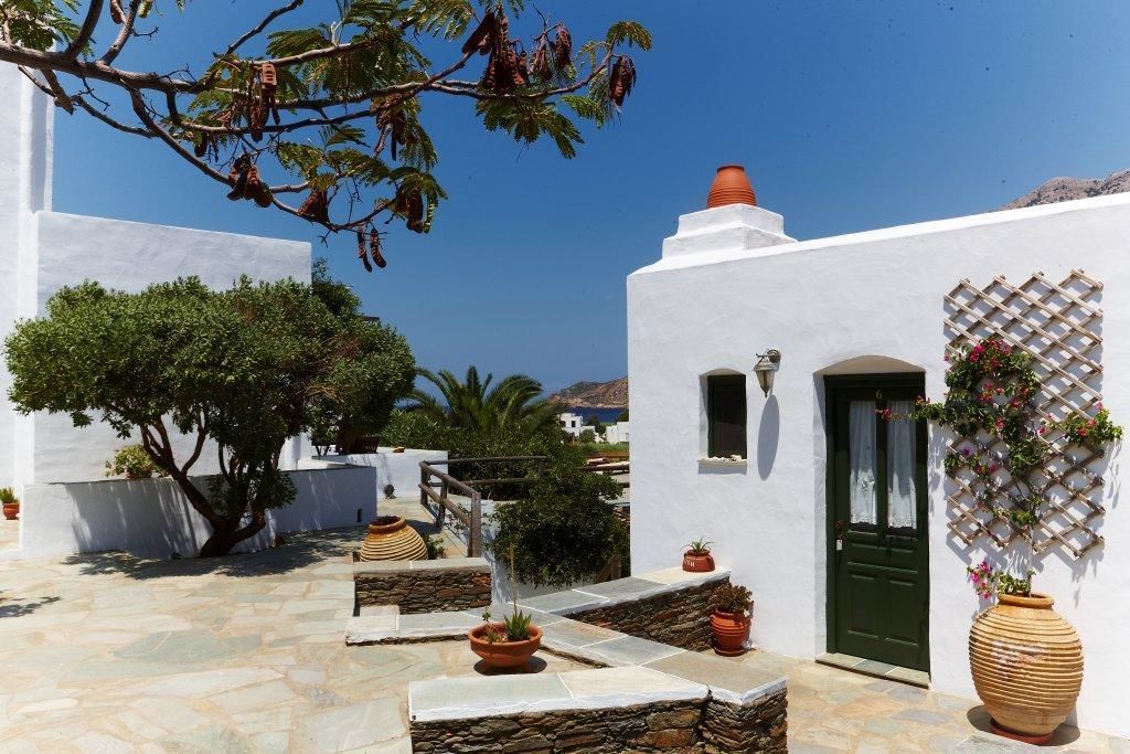 A white-walled building with a green door, stone steps, and potted plants.