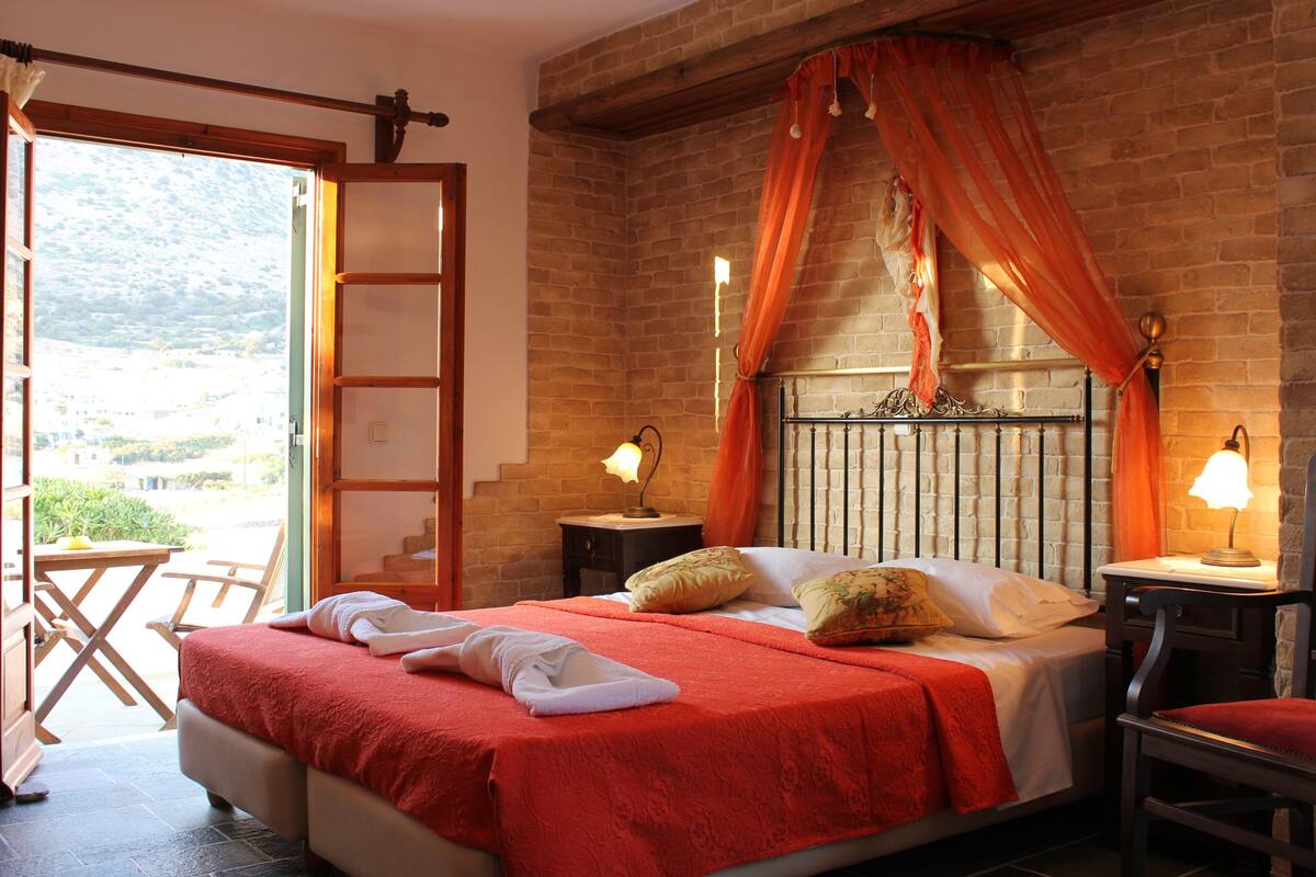 Un dormitorio con cama, mesita de noche, silla y vistas al exterior.
