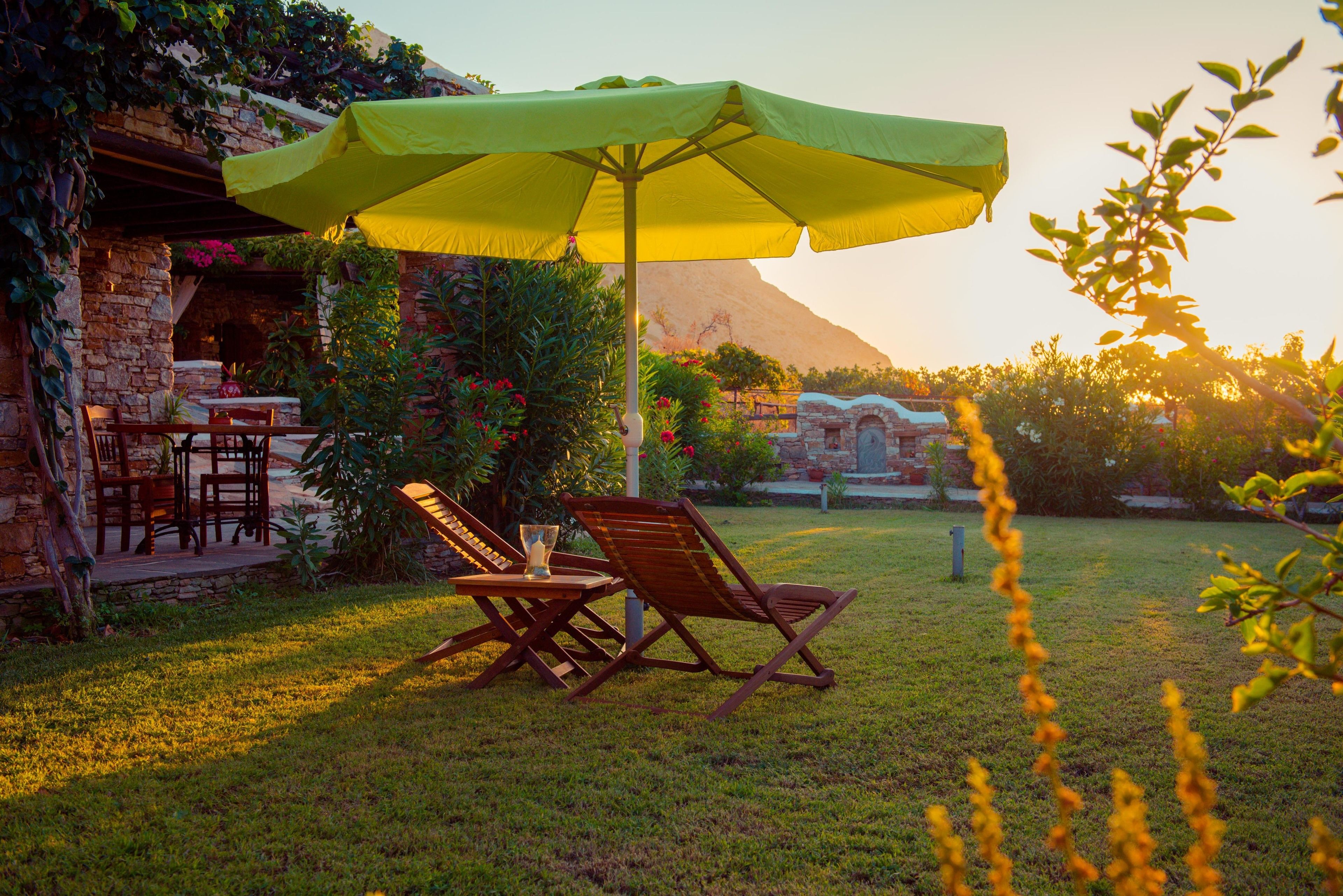 Een terras met houten stoelen en een tafel, een groene parasol, en een stenen gebouw op de achtergrond.