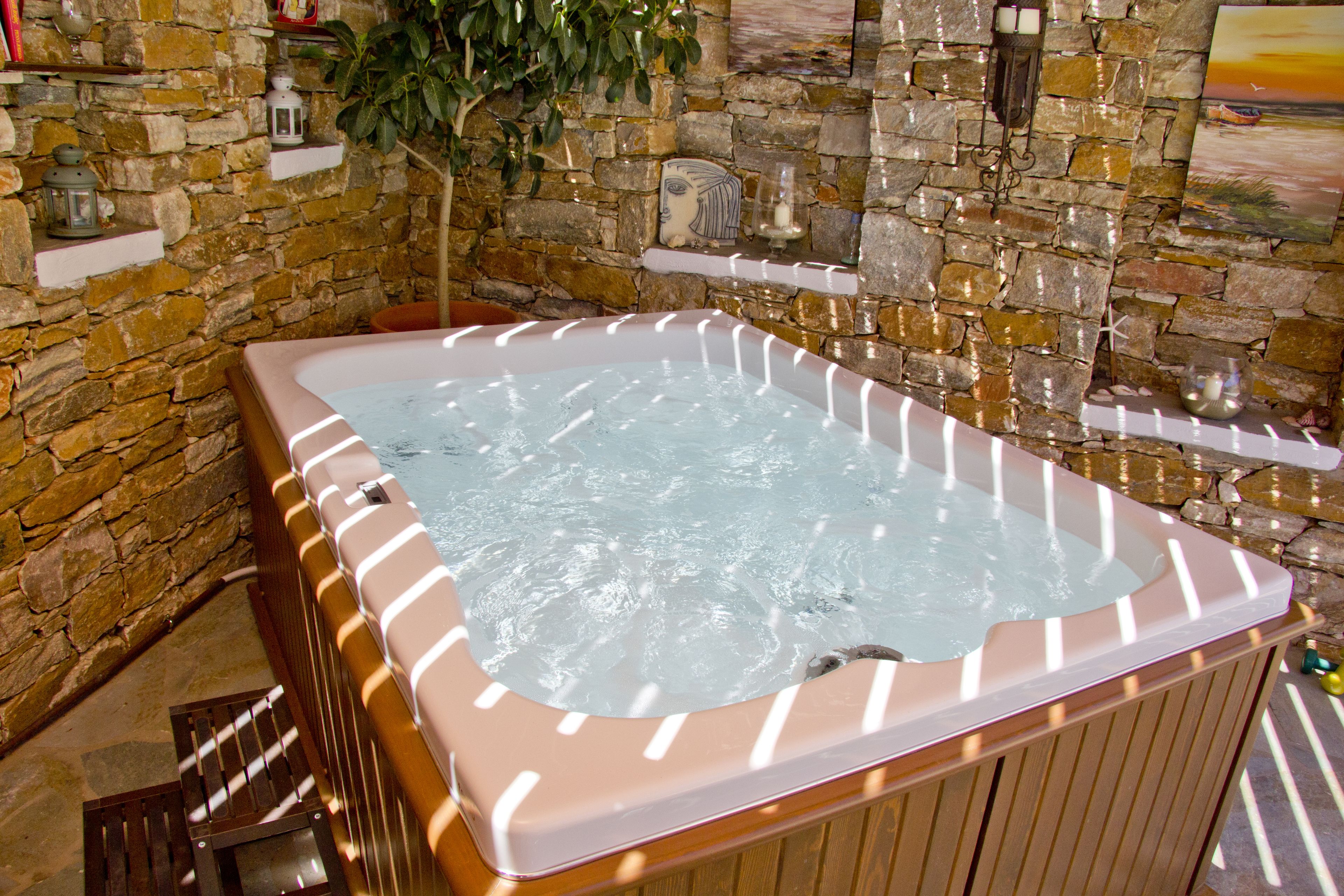 A hot tub in a stone-walled room with shelves and a plant.