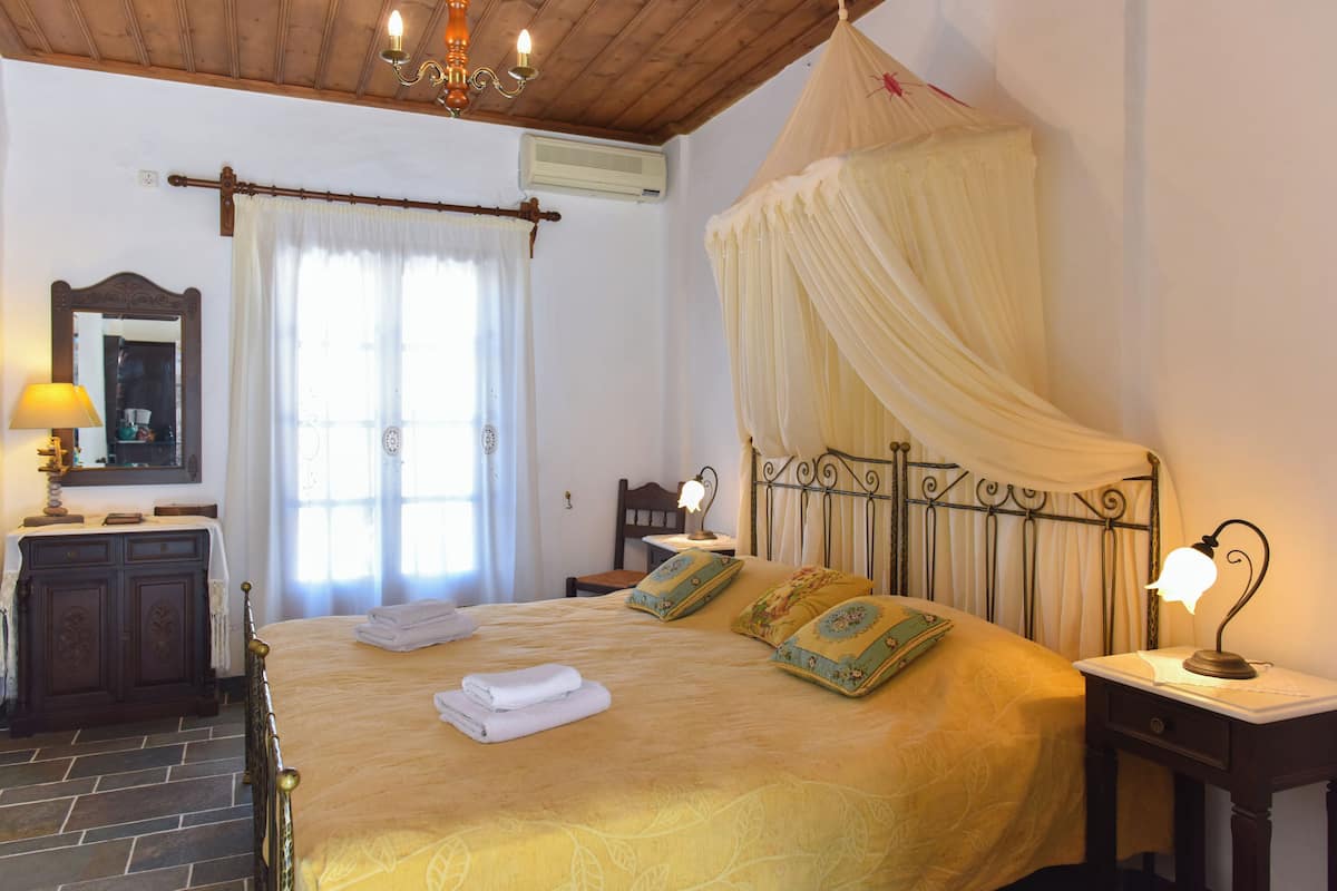 Un dormitorio con cama, mesita de noche, lámpara, espejo, armario y ventana con cortinas.