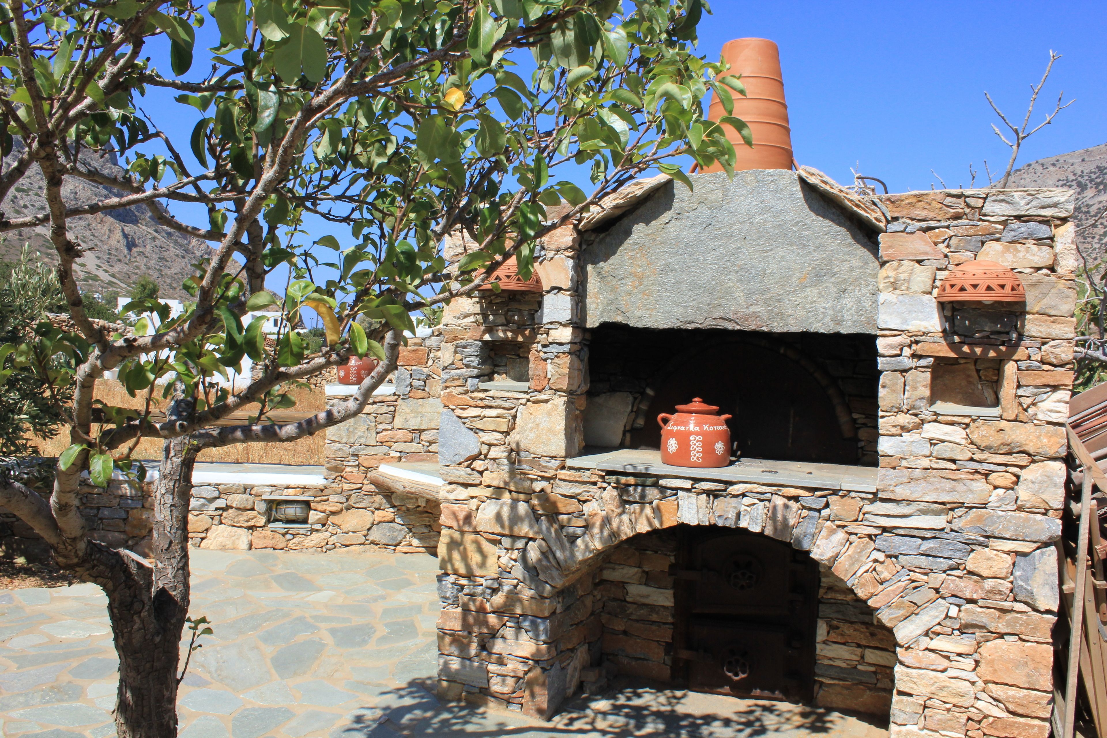 A stone-built outdoor oven with a chimney, surrounded by stone walls and a tree.