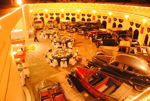Una mostra di auto d'epoca con numerosi esemplari esposti, disposti in file. In primo piano, tavoli con tovaglie bianche e sedie.