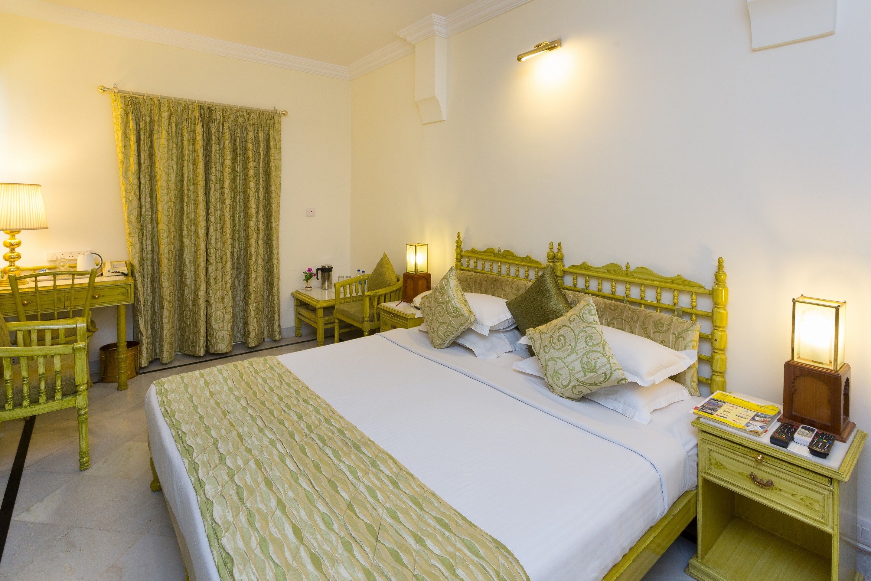 Una habitación de hotel con una cama grande, una mesita de noche con lámpara, una silla y un escritorio también con lámpara.
