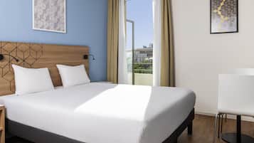 Habitación de hotel con cama, mesita de noche, escritorio, una silla y vistas al exterior.