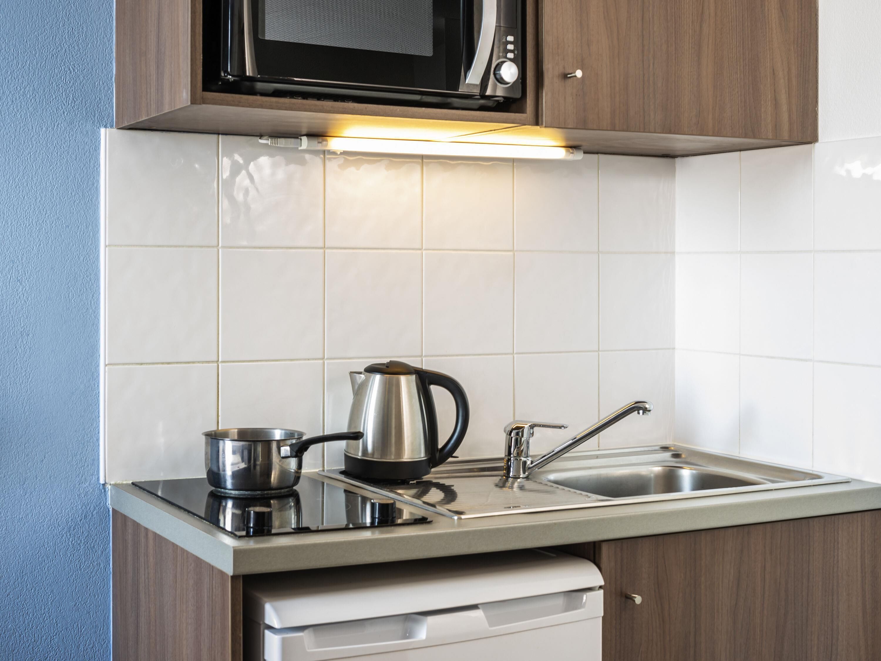 Una cocina con microondas, hervidor y pileta.