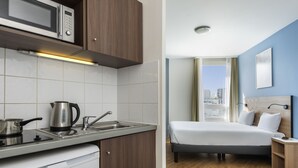 A compact hotel room with a kitchenette, a bed, a bedside table, and a view of the city. - Aparthotel Adagio Access Paris Quai D'Ivry (Ivry-sur-Seine)