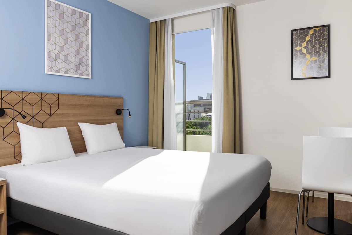 Ein Hotelzimmer mit Bett, Schreibtisch, Stuhl und Blick ins Freie.