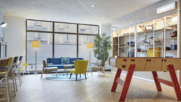 A modern library with wooden floors, a blue sofa, yellow chairs, and a red play table. - Aparthotel Adagio Access Paris Quai D'Ivry (Ivry-sur-Seine)
