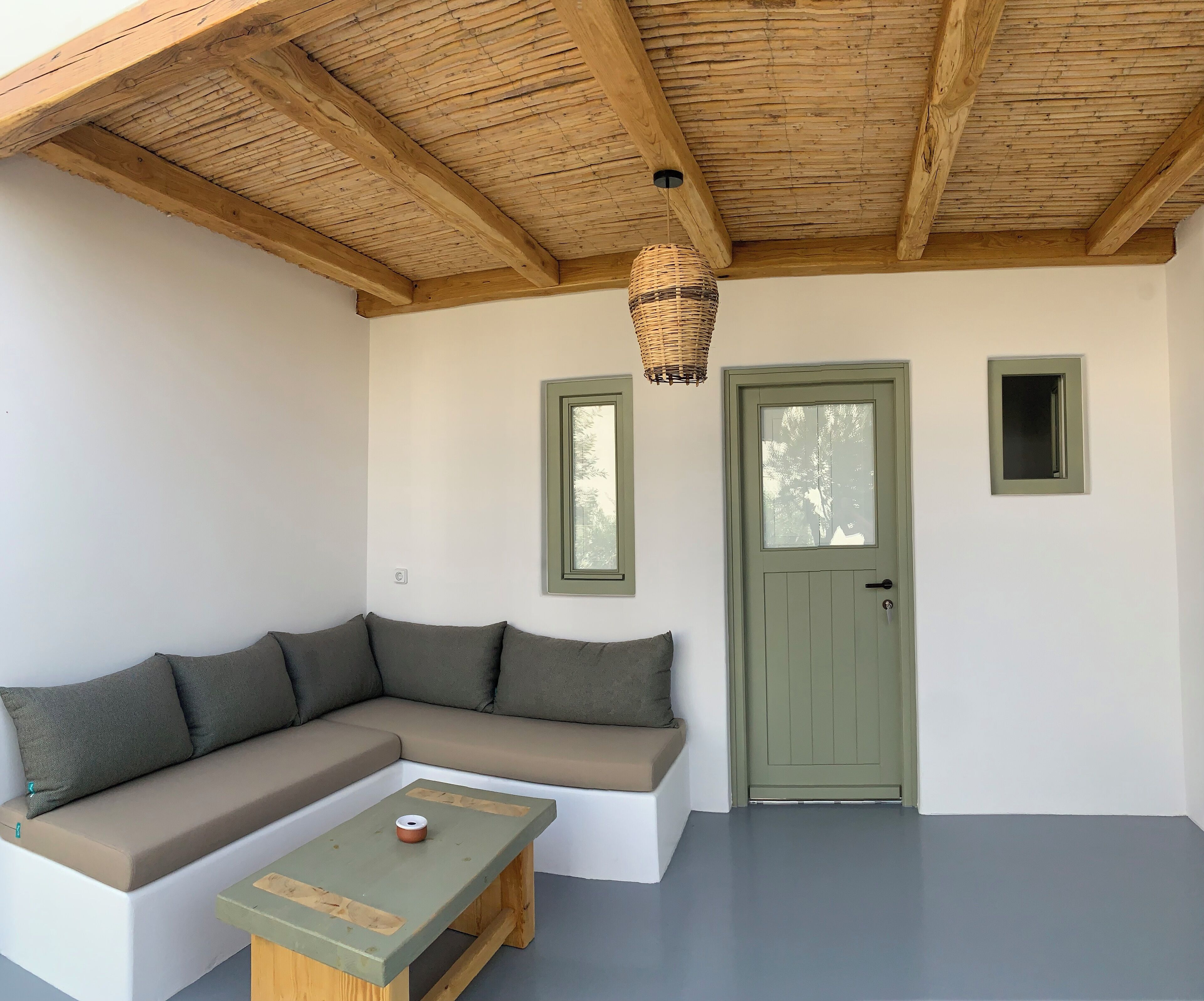 A room with a wooden ceiling, a green door, a white wall, and a grey floor.