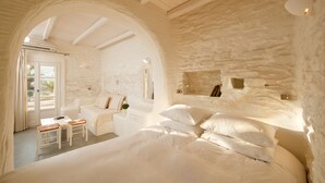 A room with a large bed, a small table, and a sofa. There is a window with curtains and a door leading outside.