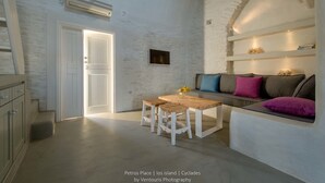 A cozy interior with a wooden table and chairs, a sofa with cushions, and a white wall with a small shelf.
