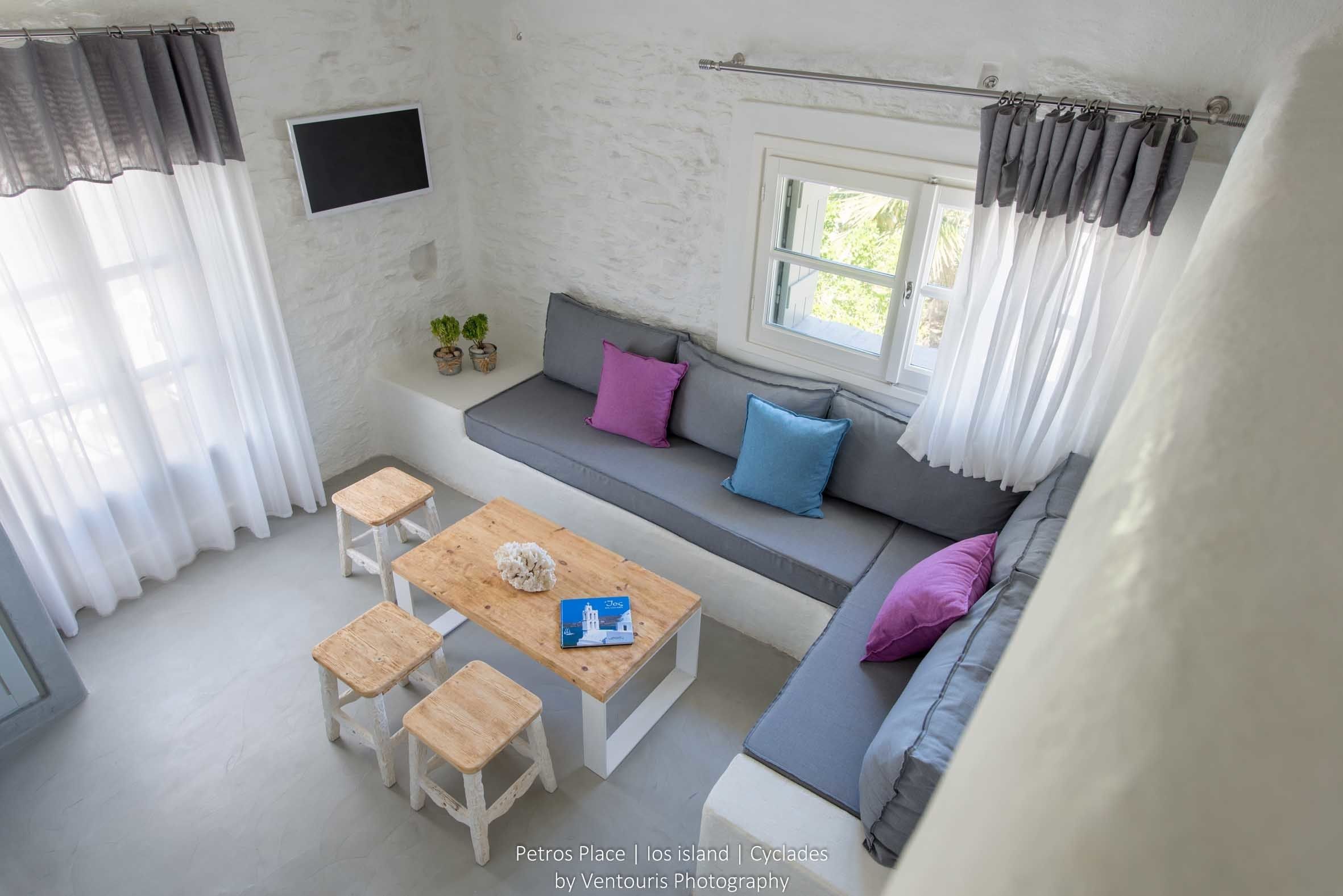 Une pièce chaleureuse avec une table en bois, quatre tabourets, un canapé avec des coussins, une fenêtre et un rideau.