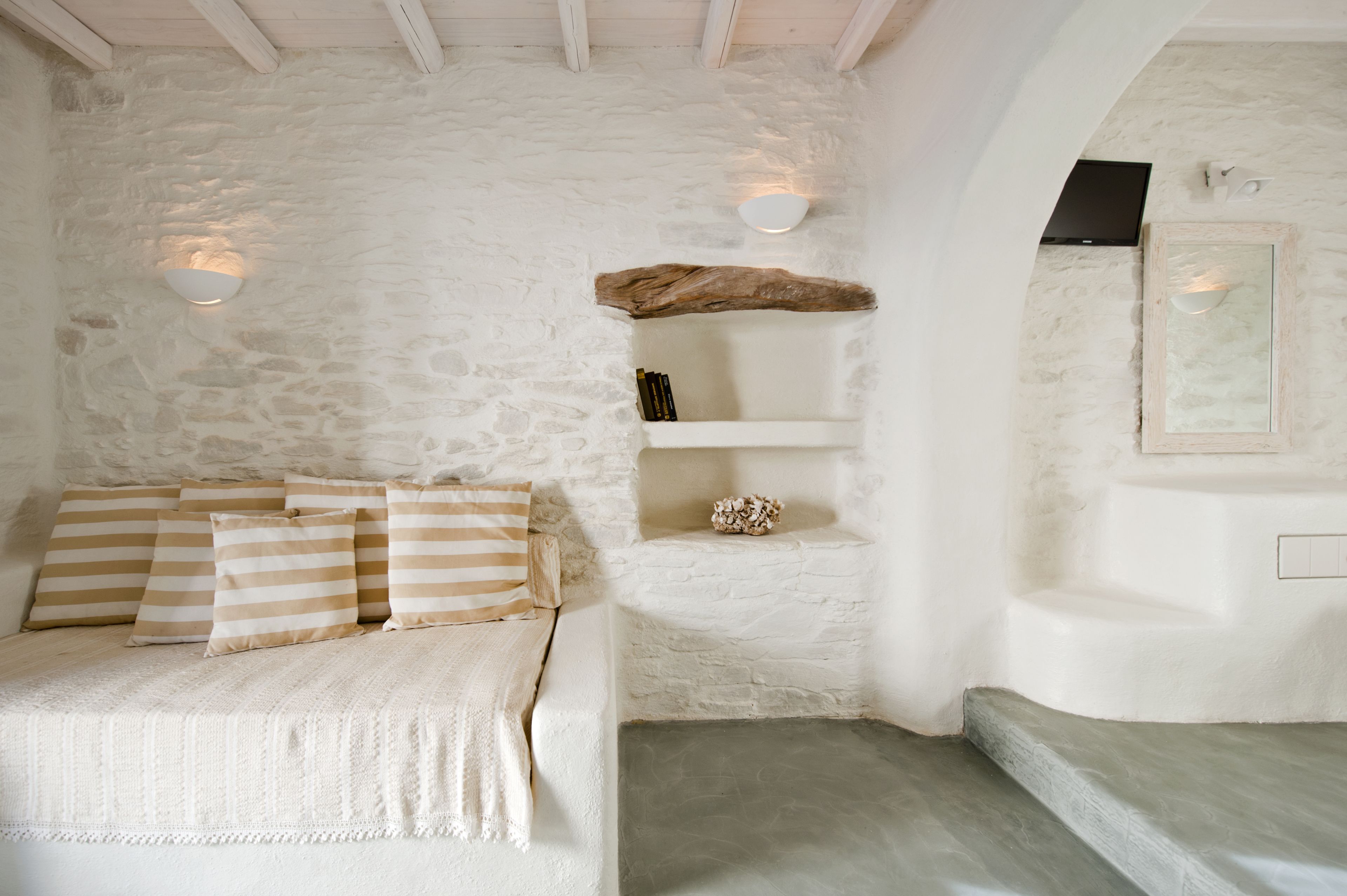 A cozy room with a stone wall, a bed with striped pillows, a shelf with decorative items, and a built-in bench.