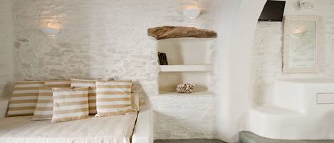 Een gezellige kamer met een stenen muur, een bed met gestreepte kussens, een plankje met decoratieve objecten en een inbouwkbank.
