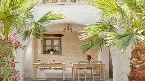 An outdoor patio with a stone table and chairs, surrounded by palm trees and flowers.