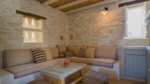 A cozy room with a stone wall, a wooden ceiling, a beige sofa with striped cushions, a small wooden table, and wicker baskets.