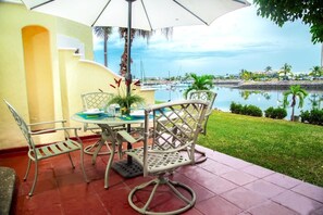 A patio with a table and chairs, a white umbrella, and a view of a marina and water. - Isla Mazatlan Residence Club (Mazatlán)