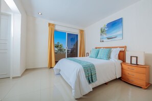 A bedroom with a bed, a nightstand, a window with curtains, and a painting on the wall. - Isla Mazatlan Residence Club (Mazatlán)