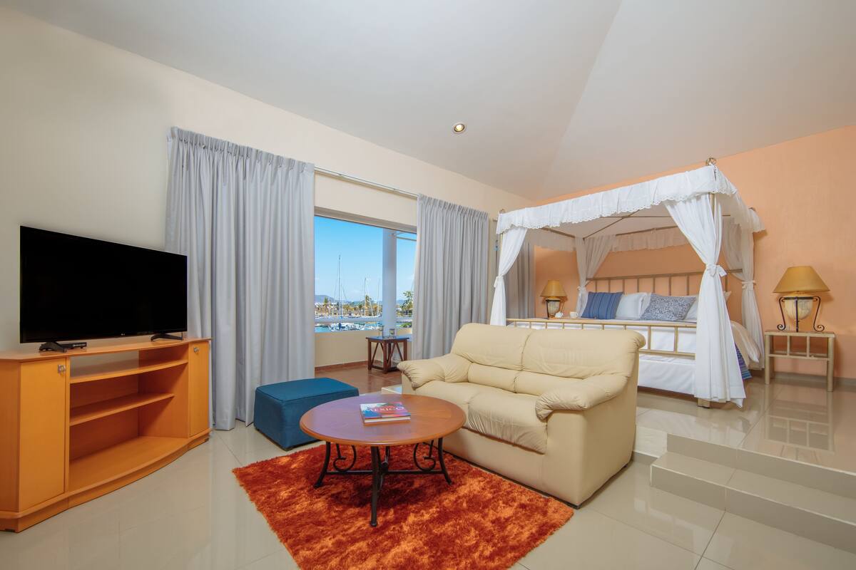 Quarto de hotel com televisão, sofá, mesa de centro e cama com dossel.