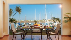 Comedor con mesa para cuatro, con vista a un puerto deportivo con barcos y palmeras.