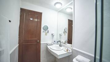 Un bany amb una porta de fusta, un lavabo blanc, un mirall i un penjallatotres.