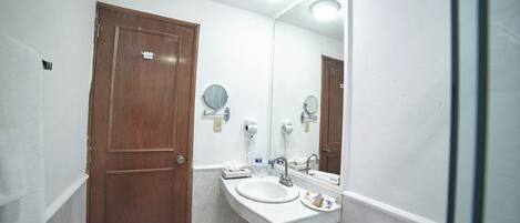 Un baño con puerta de madera, un lavabo blanco, un espejo y un perchero para toallas.