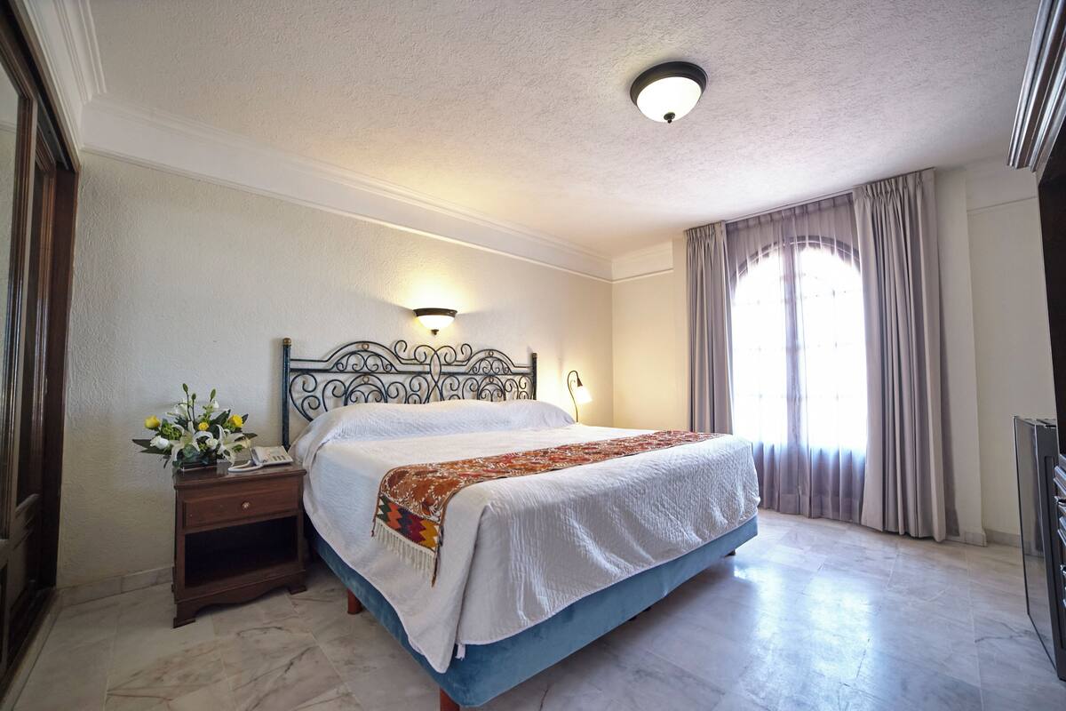 A bedroom with a bed, nightstand, lamp, and a window with curtains.