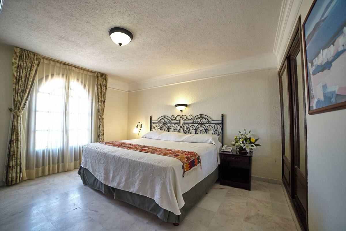 A bedroom with a bed, a nightstand, a lamp, and a painting on the wall.