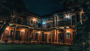 A two-story building with a courtyard, featuring columns, balconies, and potted plants.