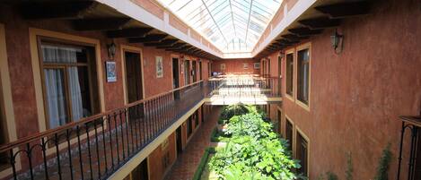 A covered courtyard with a central garden, wooden railings, and a tiled floor.