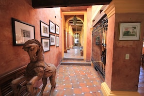 Un pasillo con una escultura de caballo de madera, cuadros enmarcados en las paredes y suelo de baldosas.