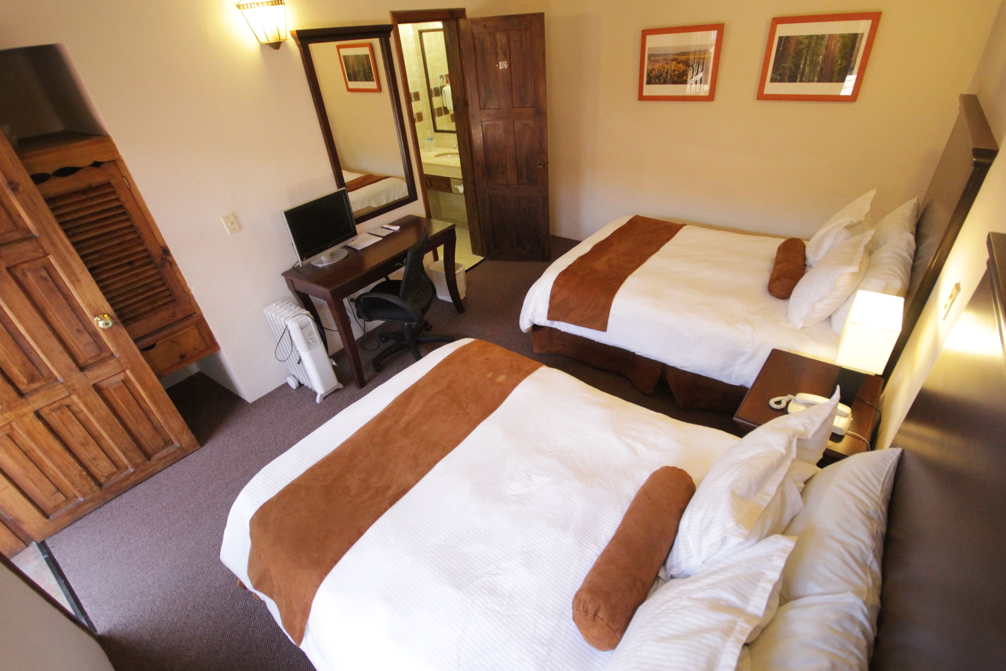 Habitación de hotel con dos camas, un escritorio, una silla, un espejo y un armario.