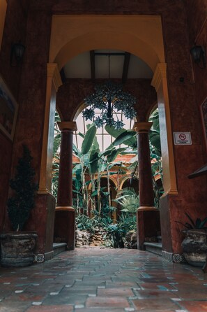 An arched corridor with columns, a tiled floor, and lush greenery. - Casa Mexicana Hotel (San Cristóbal de las Casas)