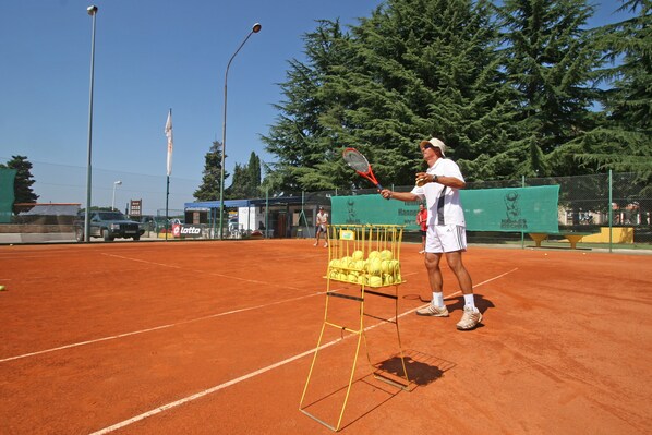 Una cancha de tenis con un hombre sosteniendo una raqueta y una cesta de pelotas de tenis.