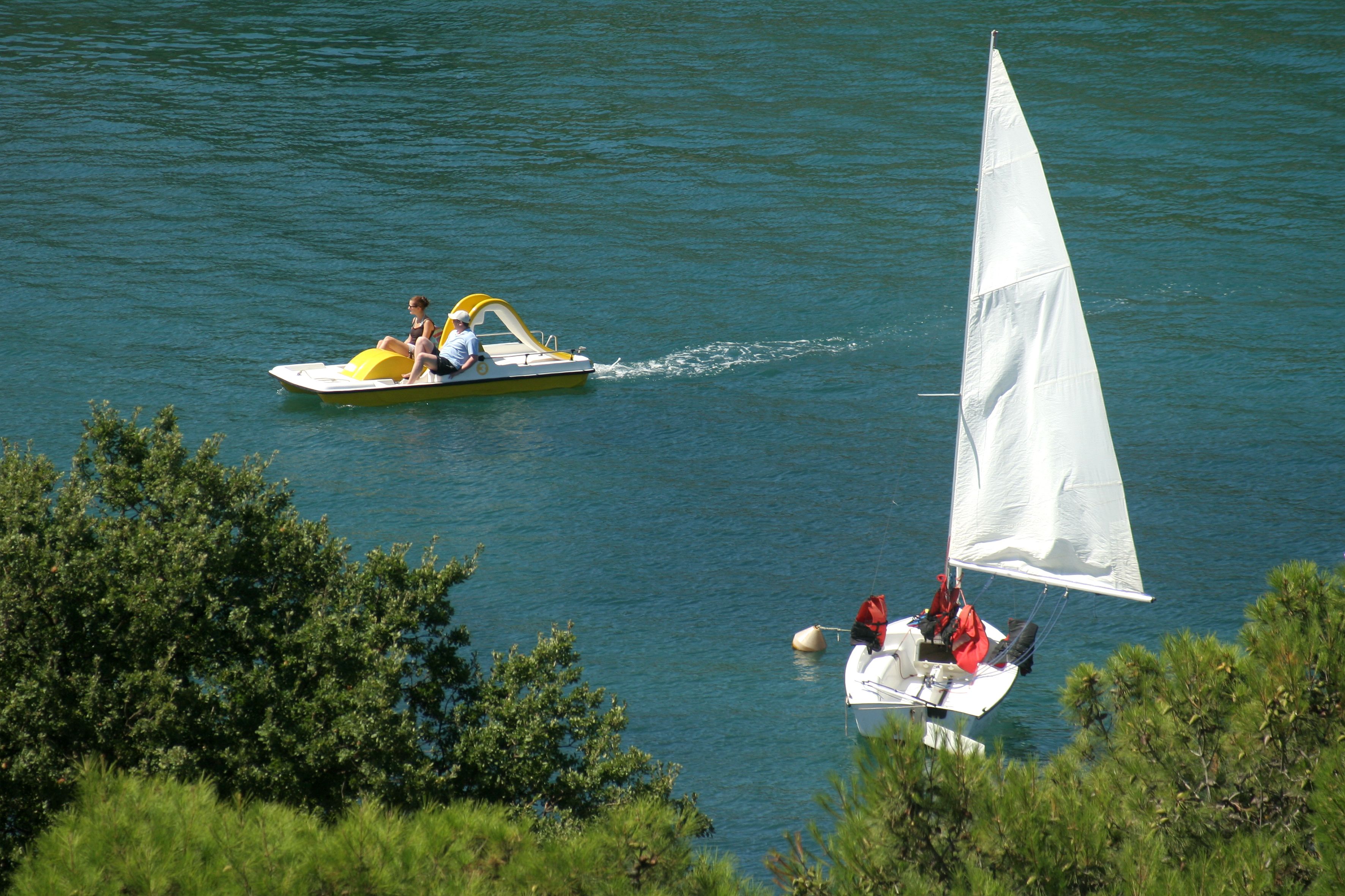 A boat with a sail and a motorboat with two people.