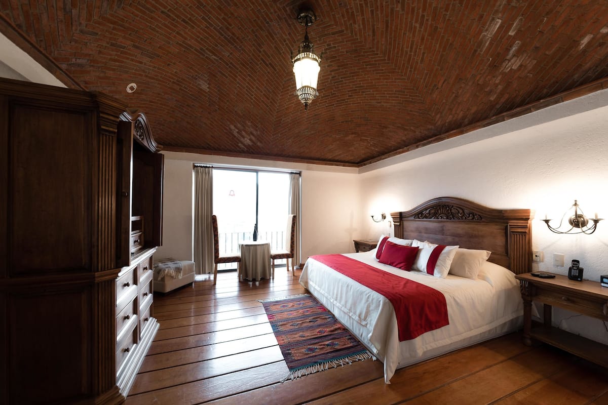 Un dormitorio amplio con una cama grande, suelo de madera, techo de ladrillo y vistas a través de un ventanal.