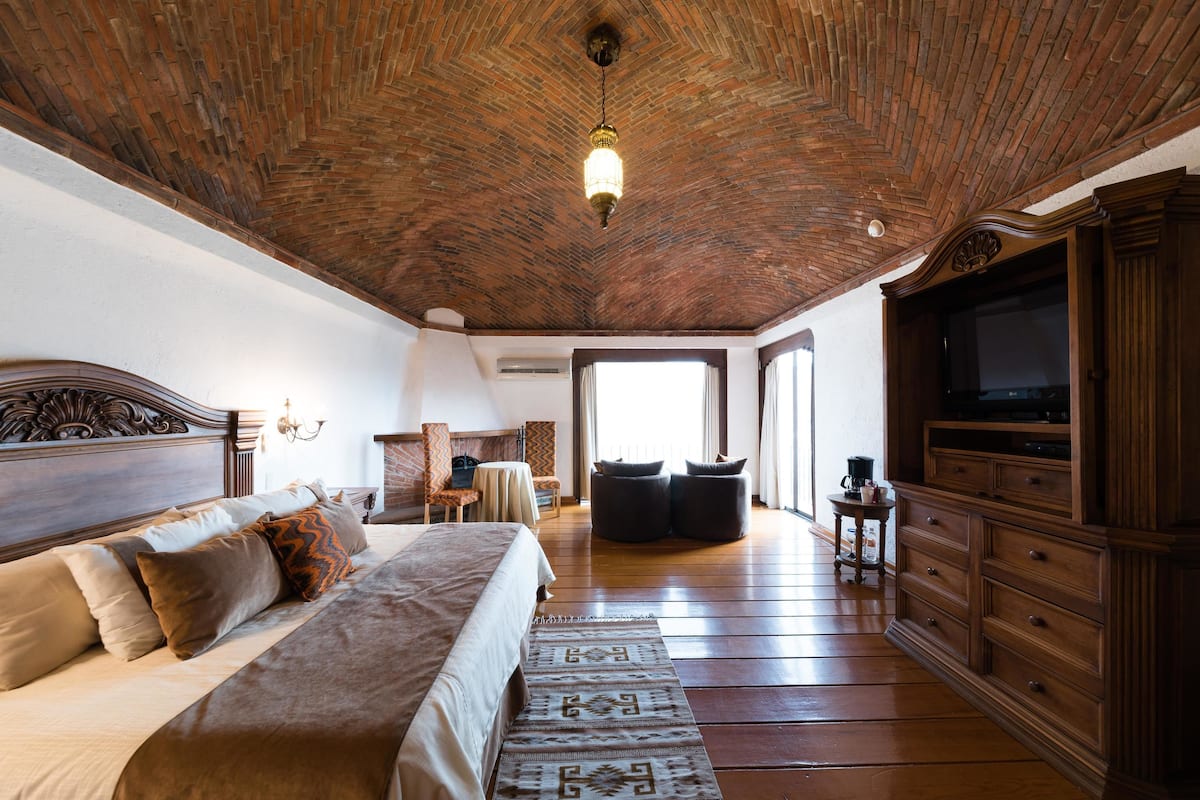 Un dormitorio espacioso con una cama grande, techo de madera y un televisor sobre un mueble de madera.