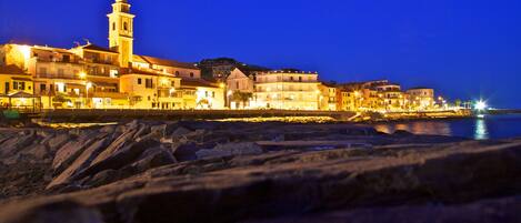 A coastal town at night with illuminated buildings and a prominent church tower.