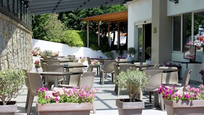 Un espace café en plein air, doté de nombreuses tables et chaises, et agrémenté de plantes et de fleurs en pot.