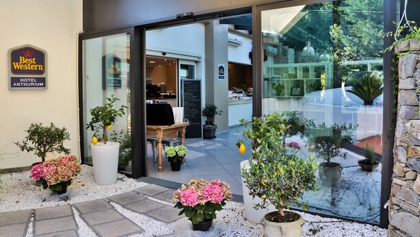 L’extérieur de l’hôtel Best Western Anthurium se distingue par son entrée en verre, ses plantes en pot et son espace café bien visible.