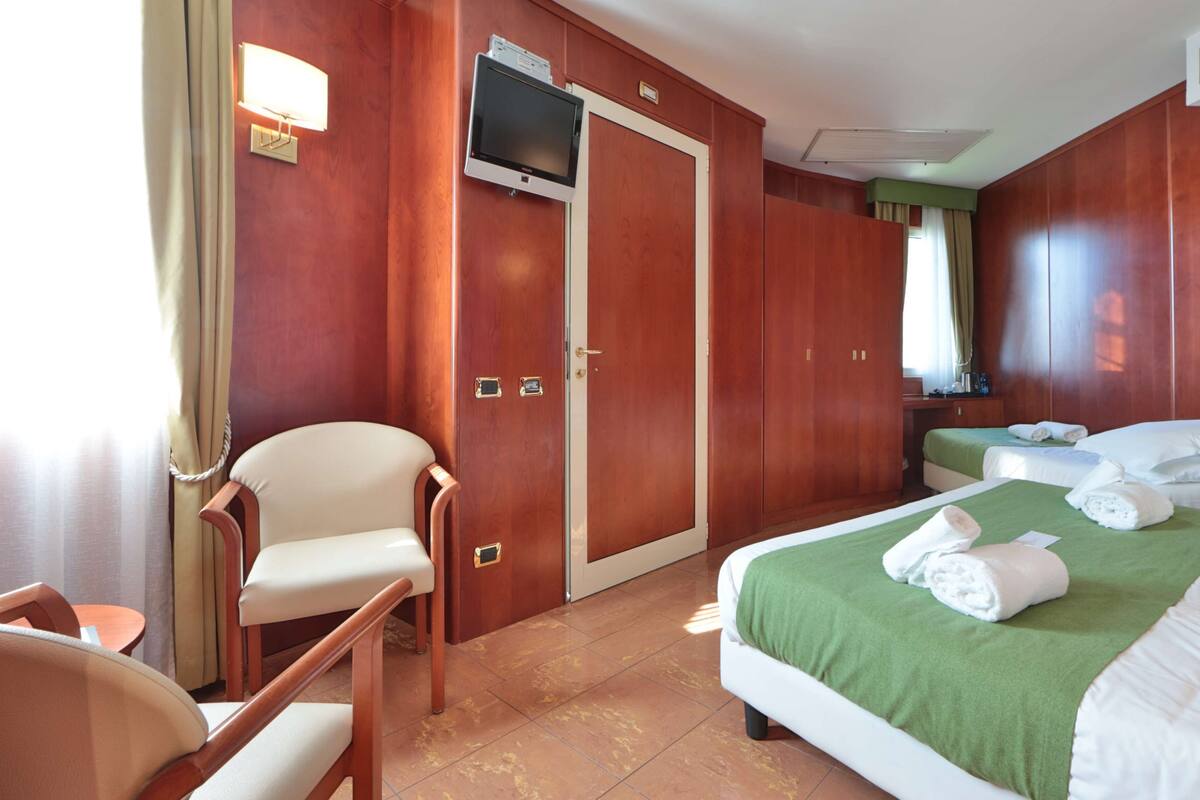 Hotellihuone, jossa on kaksi sänkyä, televisio, työpöytä ja tuoli.